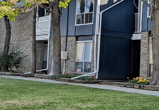 Charming two-story apartment building with classic brick facade, surrounded by lush greenery and vibrant flowers, offering a peaceful residential setting.