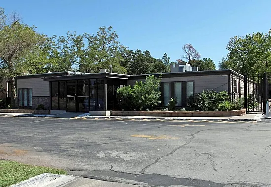 Inviting single-story building surrounded by lush greenery, featuring modern glass entrance and ample parking space.