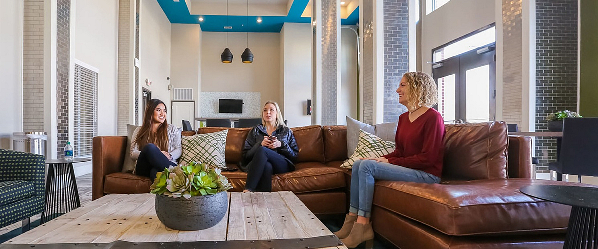 Modern apartment communal area with high ceilings, stylish chandeliers, and cozy leather sofas, creating an inviting space for relaxation and socializing.
