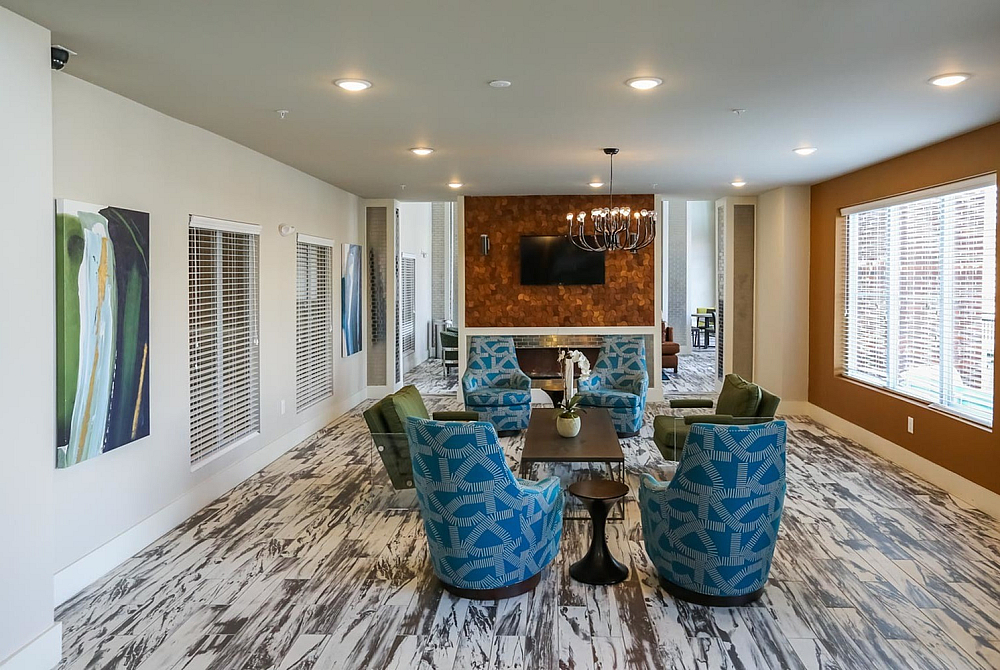 Modern lounge area featuring vibrant blue and green seating, a stylish wood-patterned floor, and a chic chandelier accentuated by a warm, textured wall.
