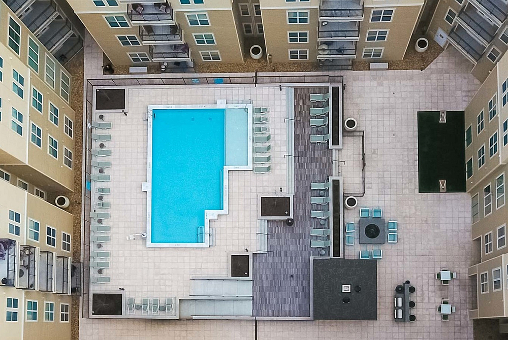 Aerial view of a vibrant apartment complex courtyard featuring a large swimming pool, multiple seating areas, and modern architectural design.