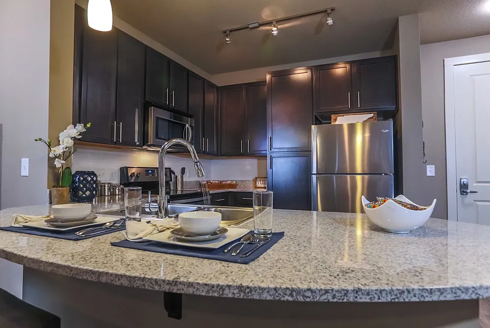 Modern kitchen with elegant dark wood cabinets, sleek granite countertops, and stainless steel appliances; inviting dining setup for two.