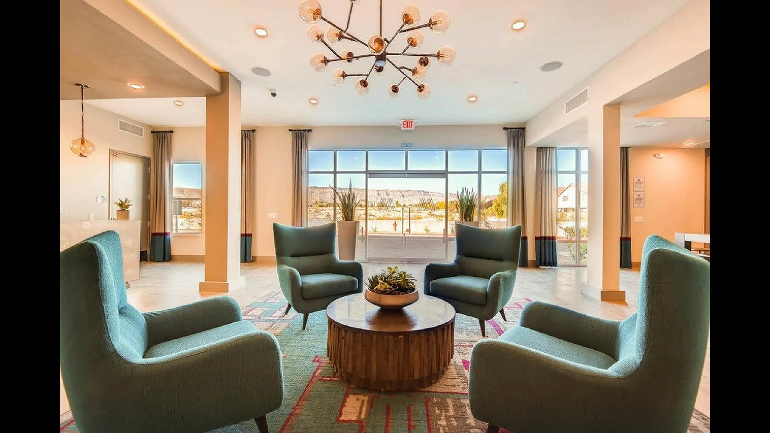 Elegantly designed open lounge area featuring stylish teal armchairs, a chic chandelier, and floor-to-ceiling windows with scenic mountain views.