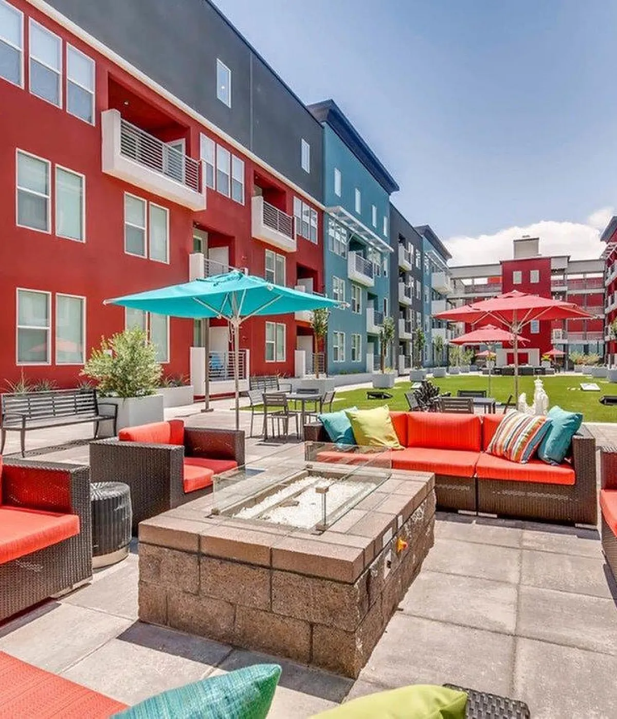 Vibrant apartment complex courtyard featuring colorful buildings, modern patio furniture, and lush green spaces with red and blue accents.