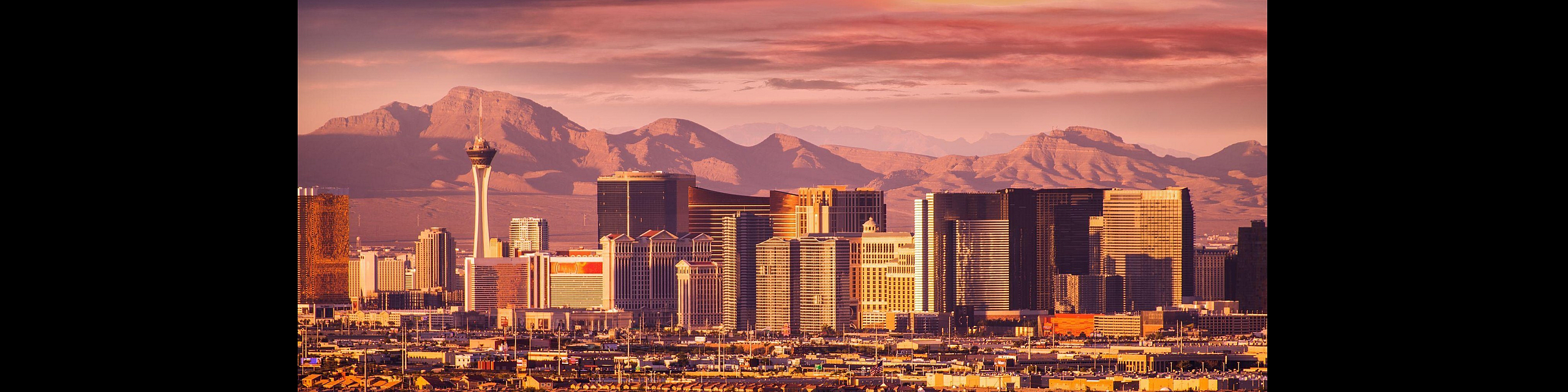 Breathtaking view of a vibrant city skyline with towering buildings set against a stunning mountain backdrop at sunset.