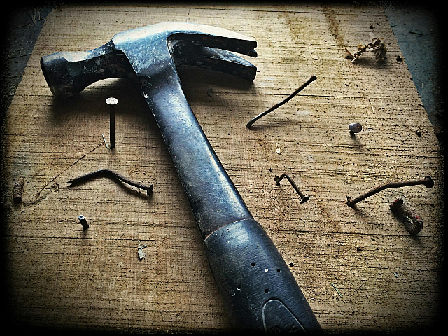 Rustic carpentry scene featuring a well-used hammer and scattered nails on a wooden surface, embodying craftsmanship and resilience.