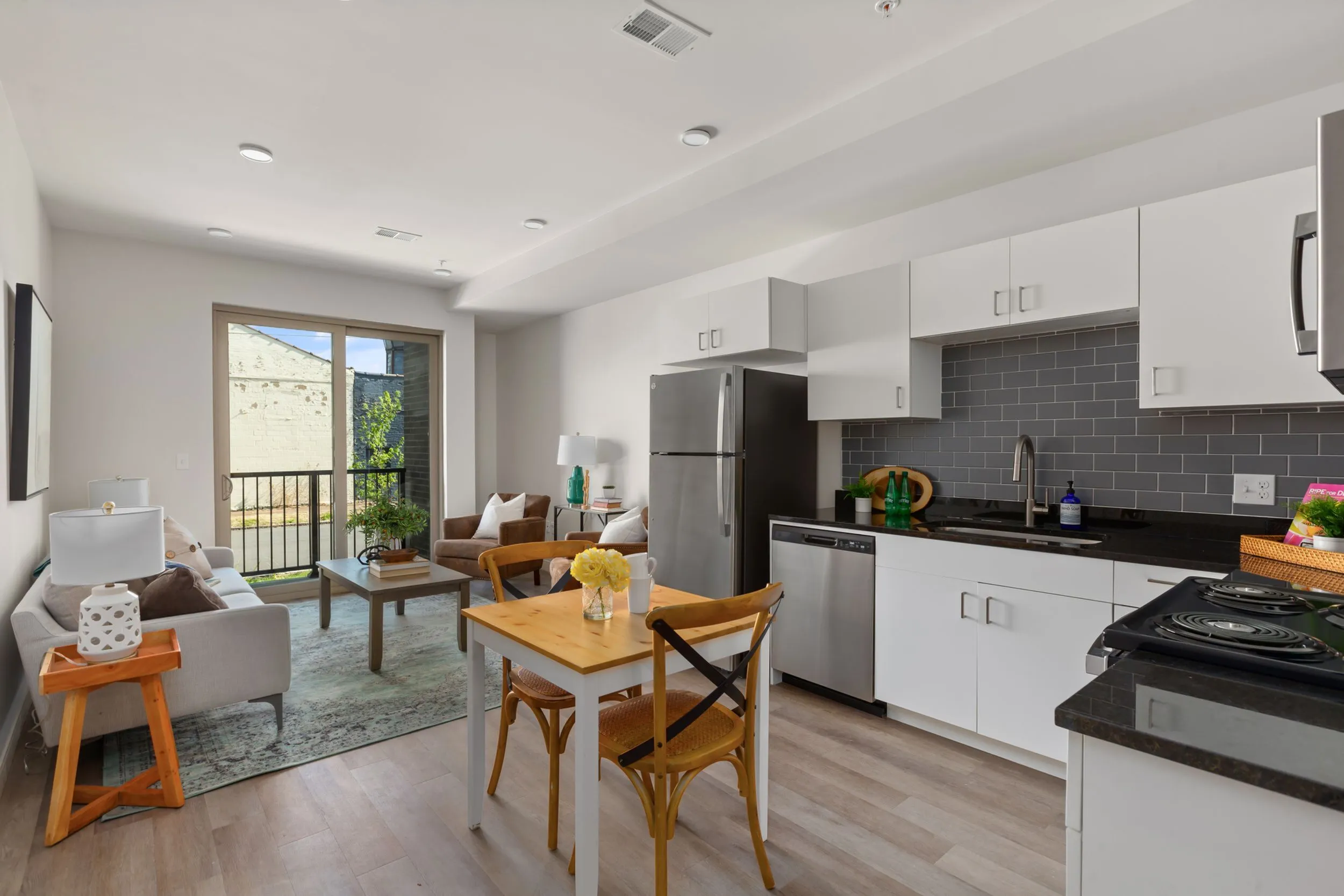 Modern apartment featuring an open-concept kitchen with sleek white cabinets and stainless steel appliances, adjacent to a cozy living area with abundant natural light.