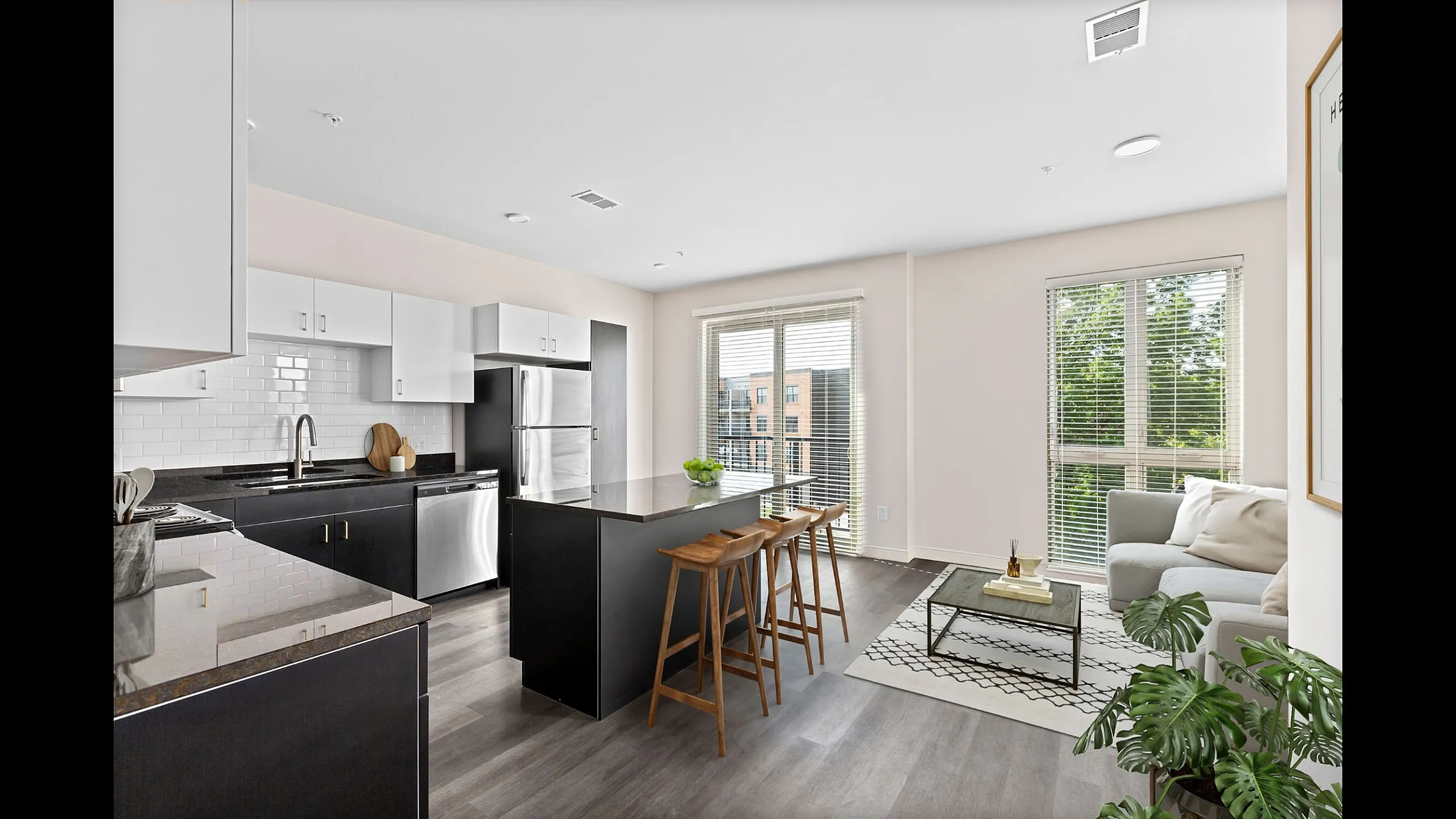 Modern open-concept kitchen and living area with sleek black and white cabinetry, stainless steel appliances, and natural light streaming through large windows.
