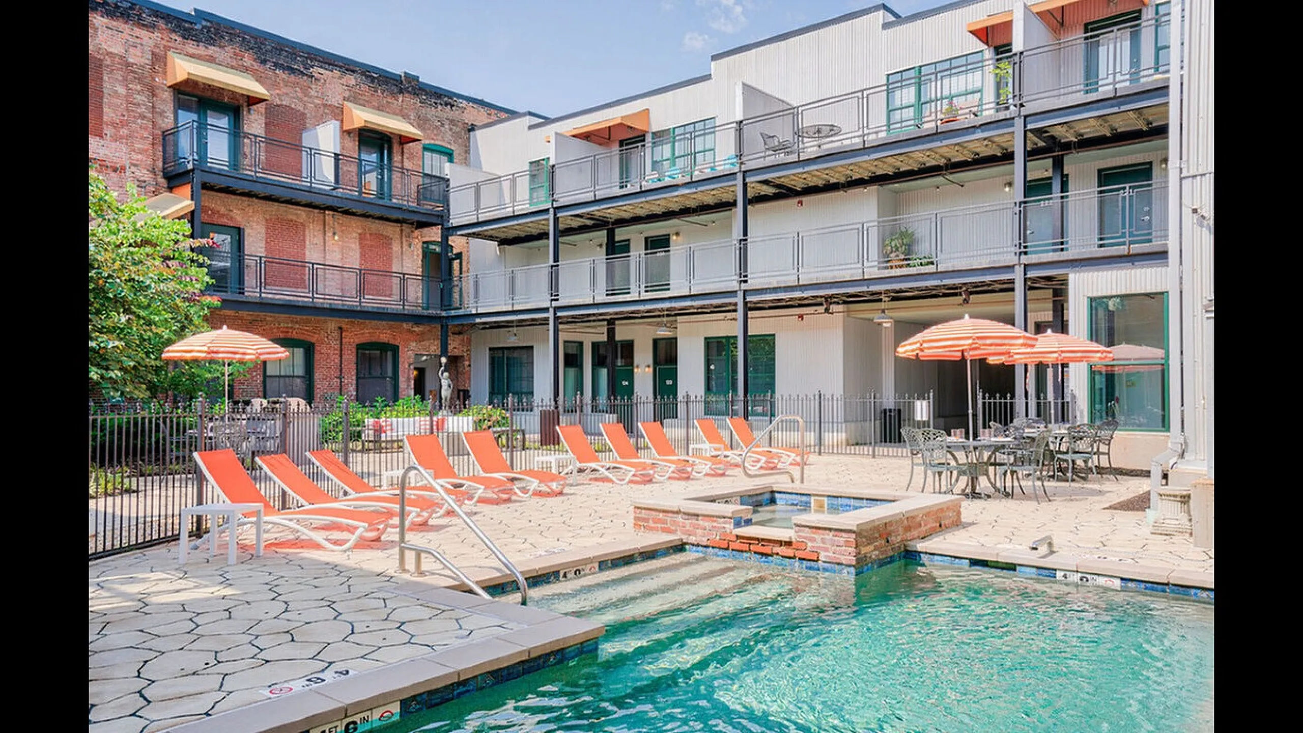 Charming apartment courtyard featuring modern balconies, vibrant orange lounge chairs, inviting pool, and chic outdoor seating with umbrellas.