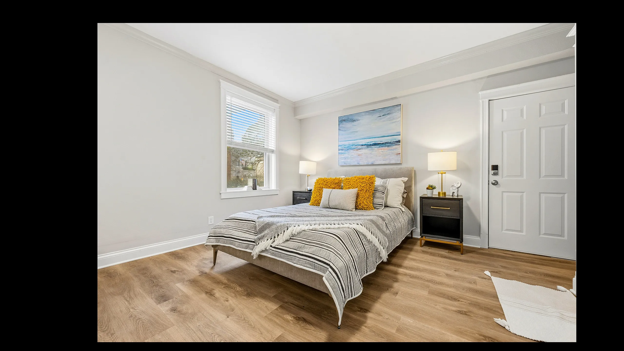 Bright and inviting bedroom with hardwood floors, cozy bed adorned with stylish pillows, and modern bedside tables with lamps.