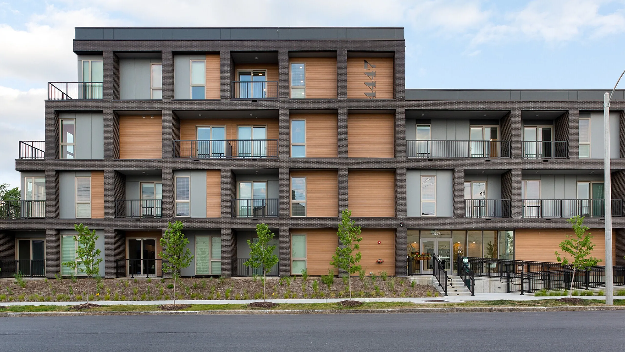 Contemporary apartment building with a modern facade, featuring private balconies and lush landscaping on a quiet street.