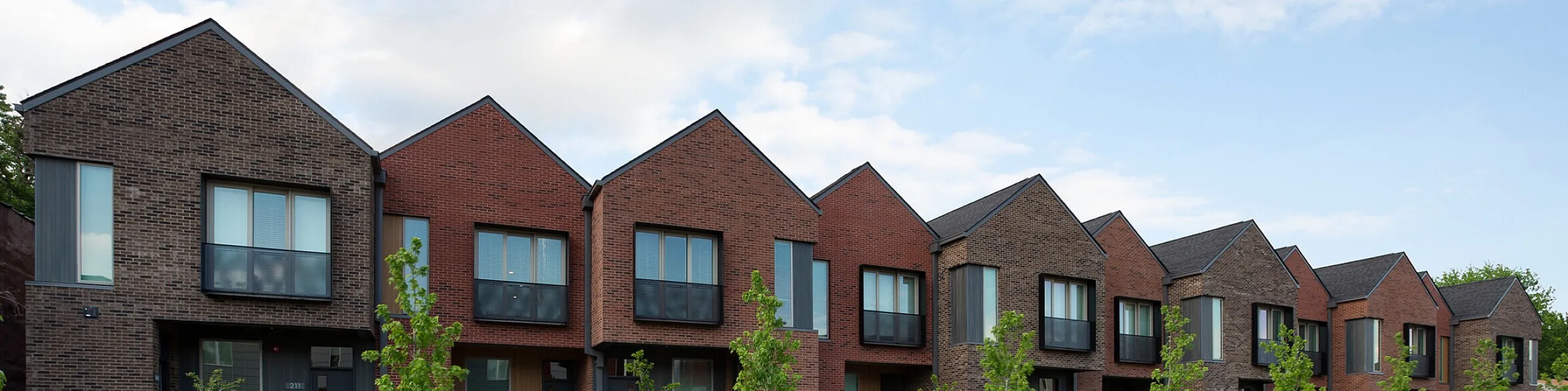 Charming modern townhouses with unique brick facades and lush greenery, showcasing contemporary urban living.