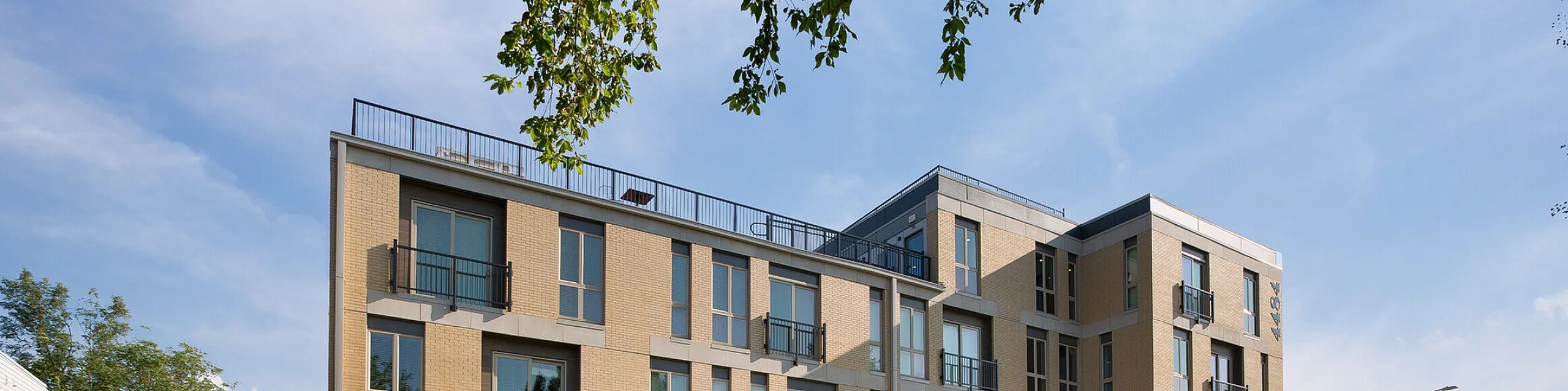 Modern apartment building with multiple balconies, large windows, and a welcoming green landscape, showcasing contemporary urban living.