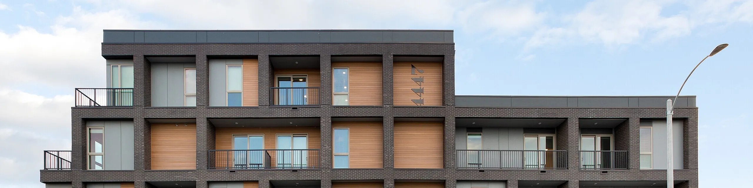 Modern four-story apartment complex with sleek balconies and large windows, surrounded by lush landscaping, offering an inviting urban living space.