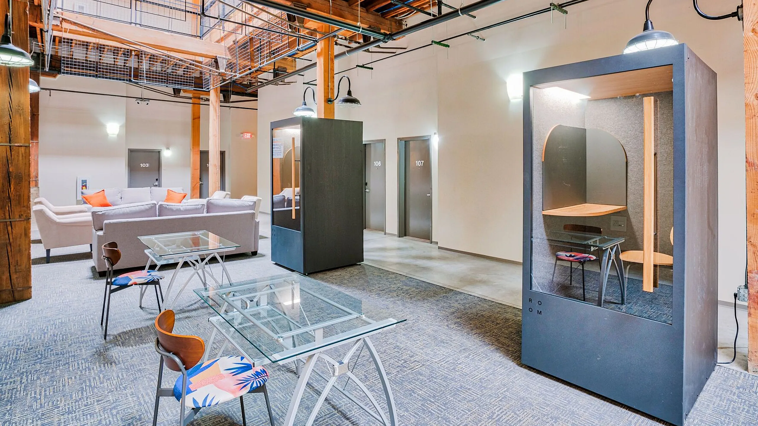 Chic loft-inspired space featuring exposed wooden beams, modern lounge area, and cozy work pods.
