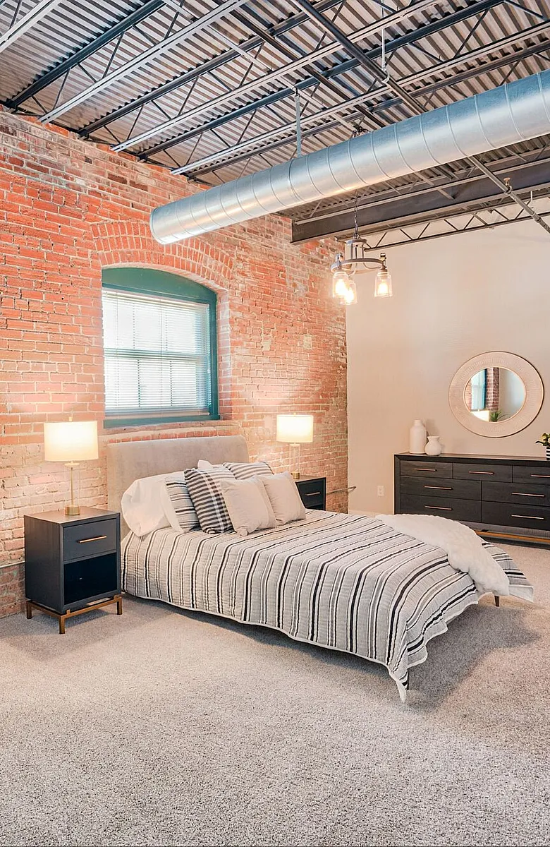 Chic industrial-style bedroom with exposed brick walls, cozy bed, and modern furnishings.