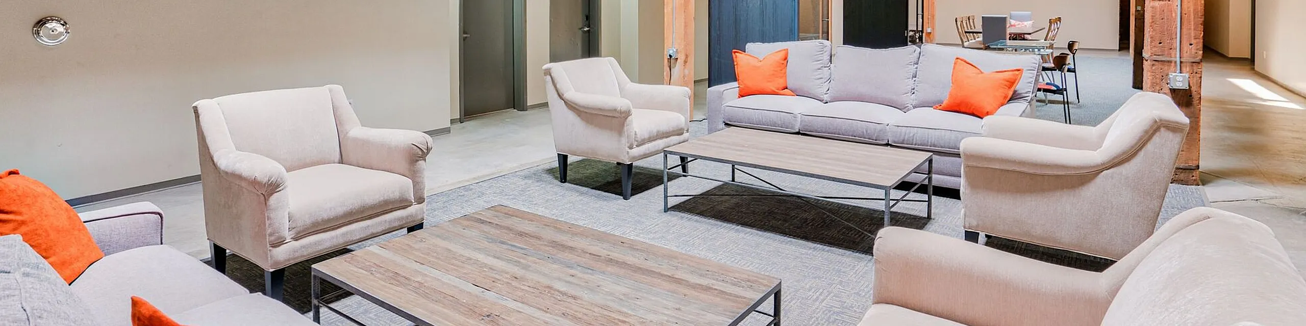 Spacious industrial loft with modern seating area, vibrant orange pillows, and stylish wooden beams.