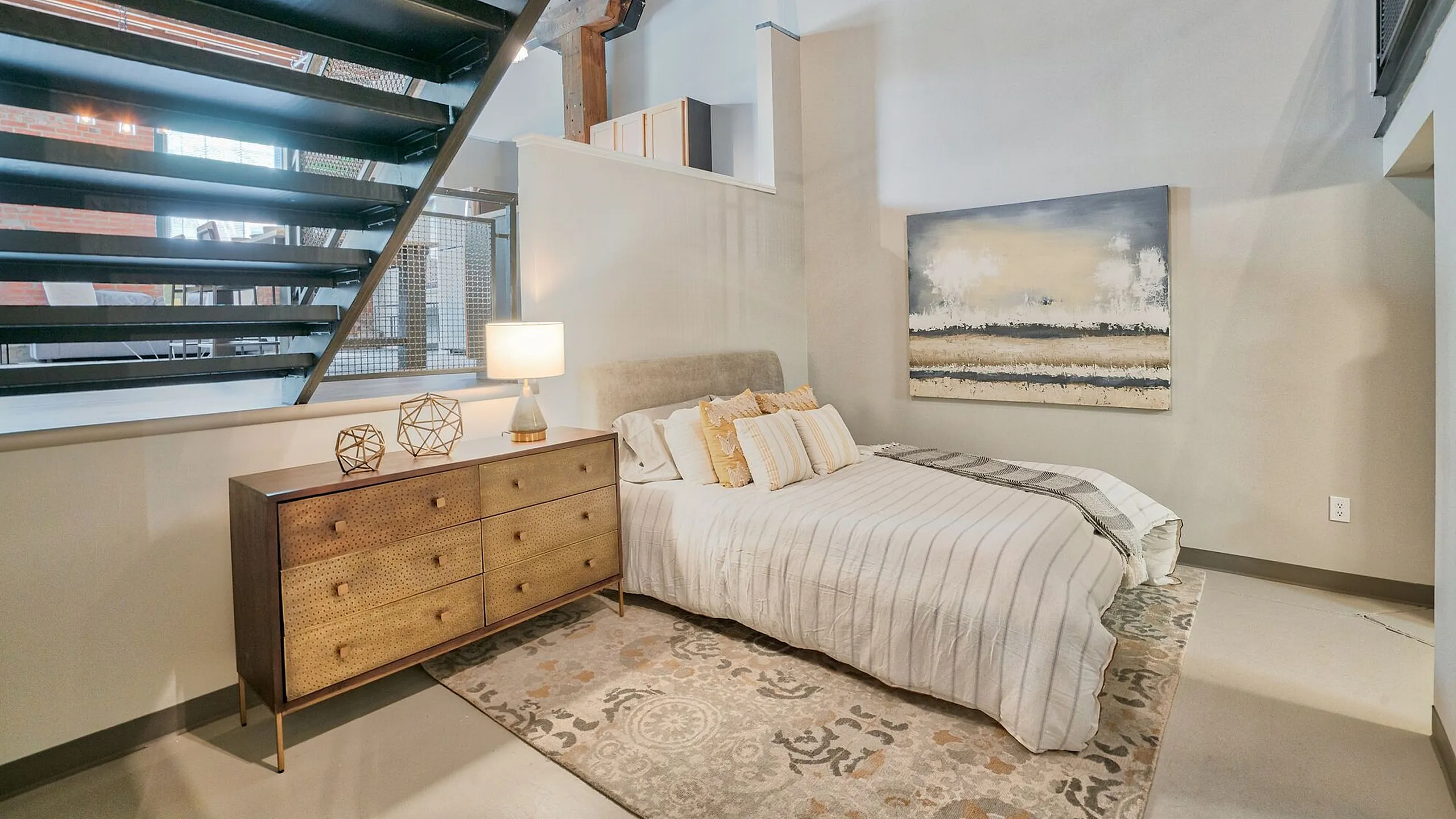 Chic bedroom with industrial loft style, featuring a cozy bed, elegant dresser, artistic decor, and a warm, inviting ambiance.