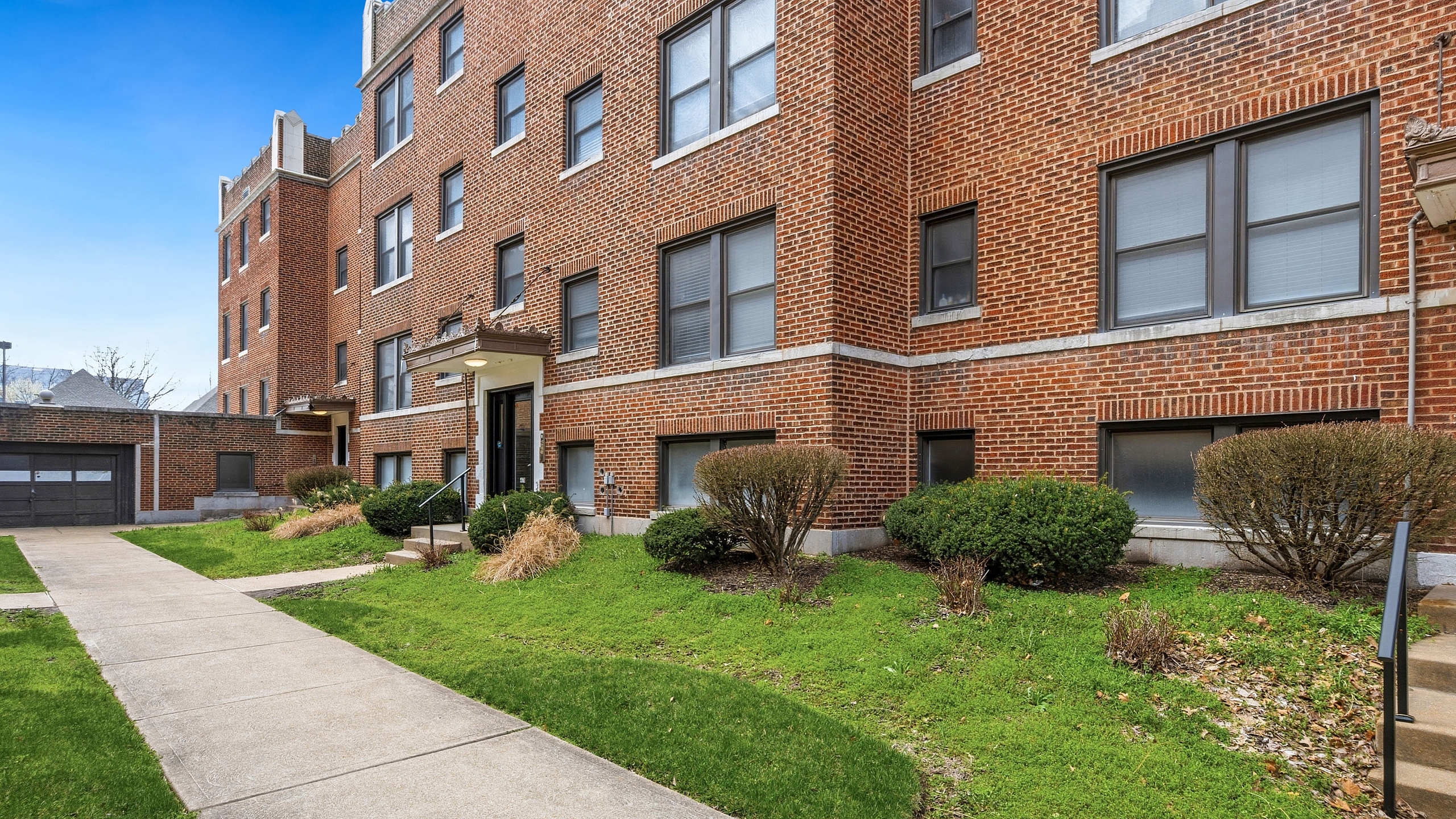 Charming brick apartment building with lush green landscaping and inviting pathways.