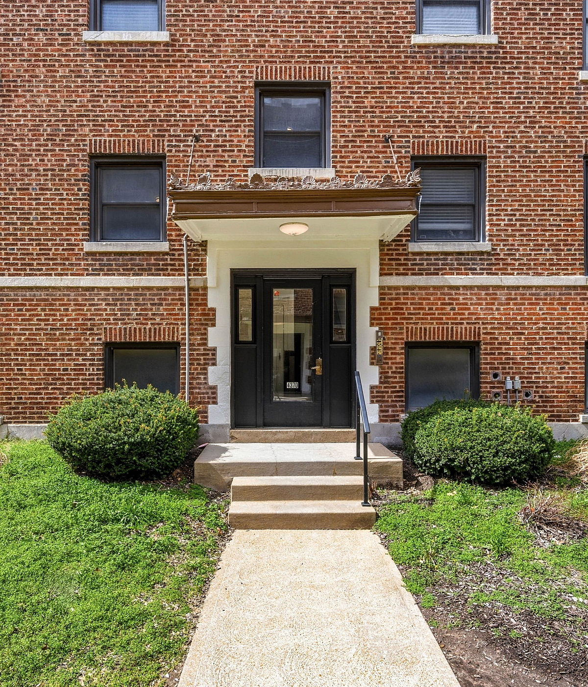 Charming brick apartment exterior with manicured greenery, inviting front entrance, and classic architectural details.
