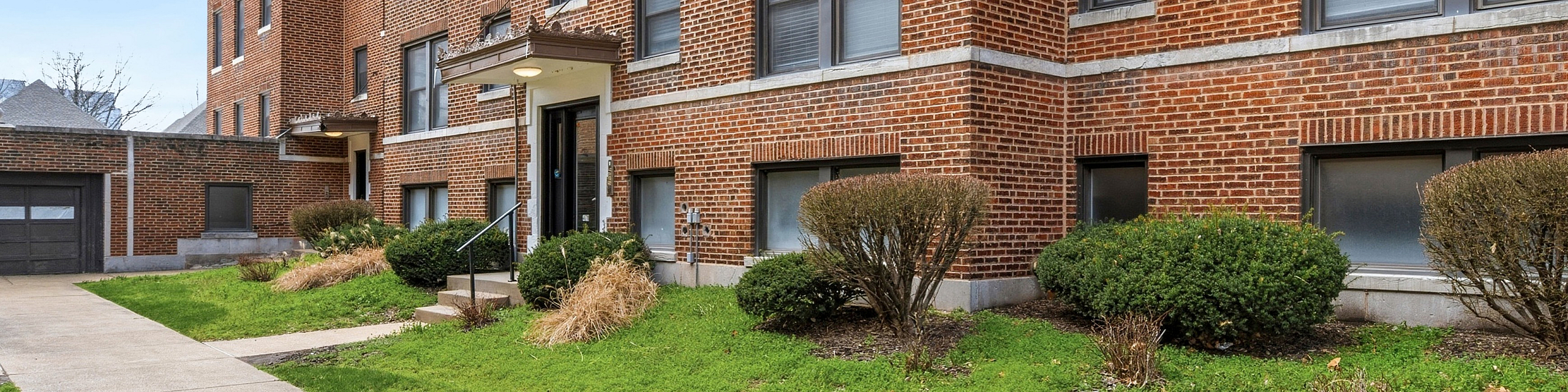 Charming brick apartment building with lush green landscaping and inviting entryway.