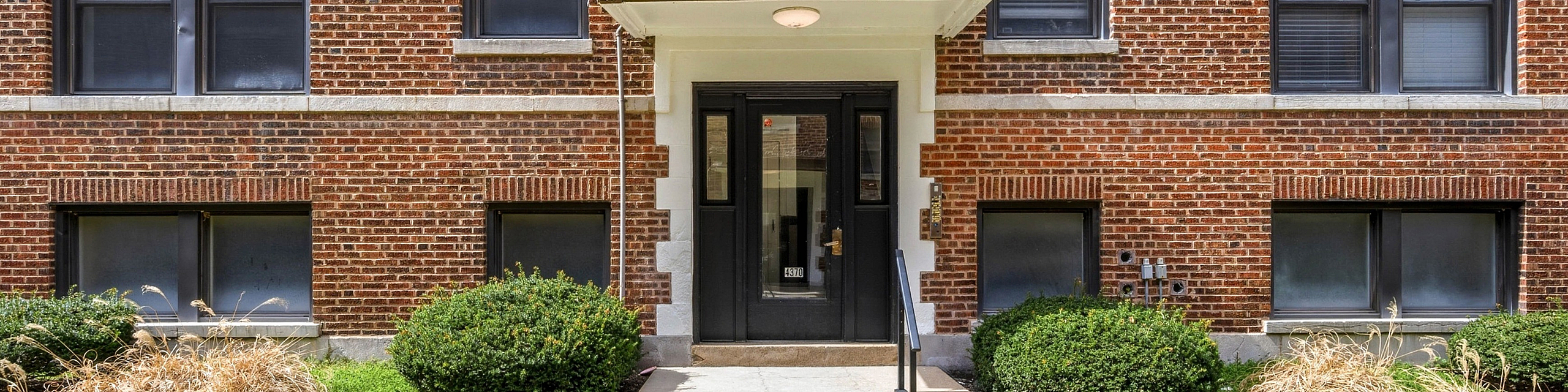 Charming brick apartment building with manicured green landscaping and classic architectural design.