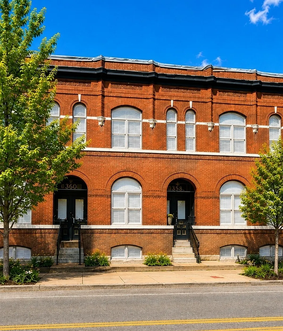 Charming red-brick apartment building featuring classic architectural details and lush landscaping, with bright blue sky above.