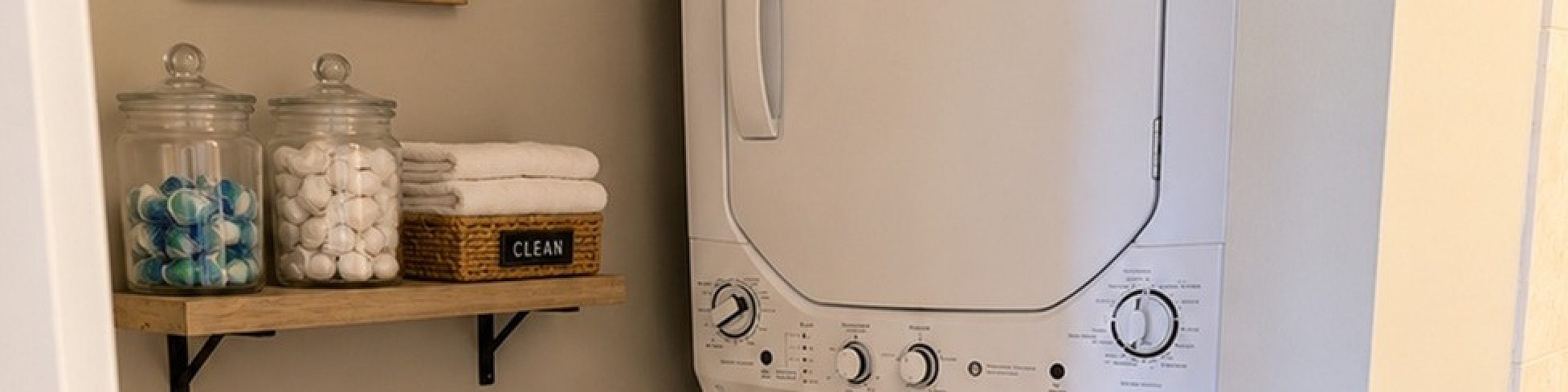 Charming laundry nook with stacked washer and dryer, wooden shelves, and chic decor.