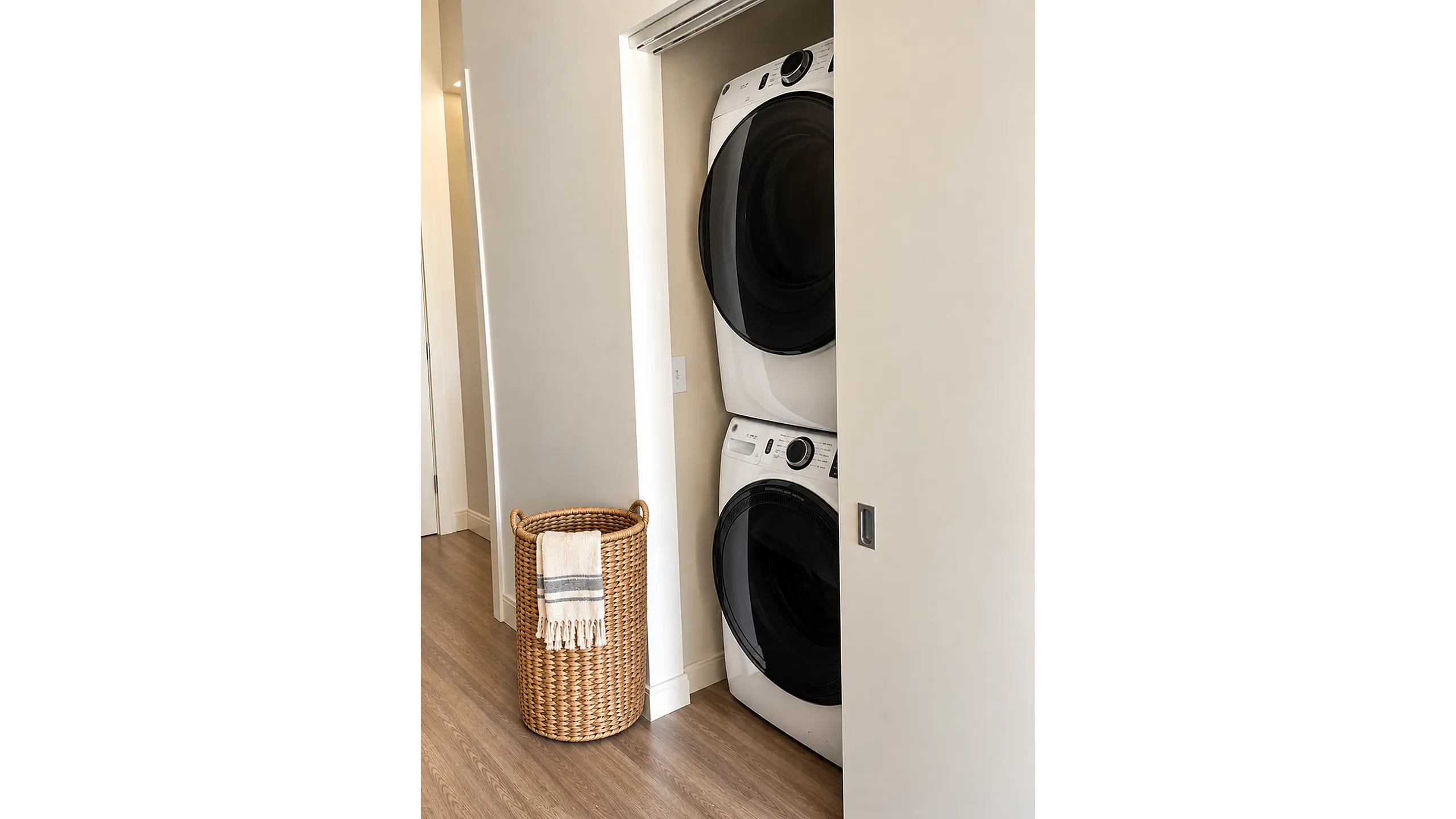 Contemporary apartment with a sleek in-unit laundry featuring a stylish stacked washer and dryer alongside a chic woven laundry basket.