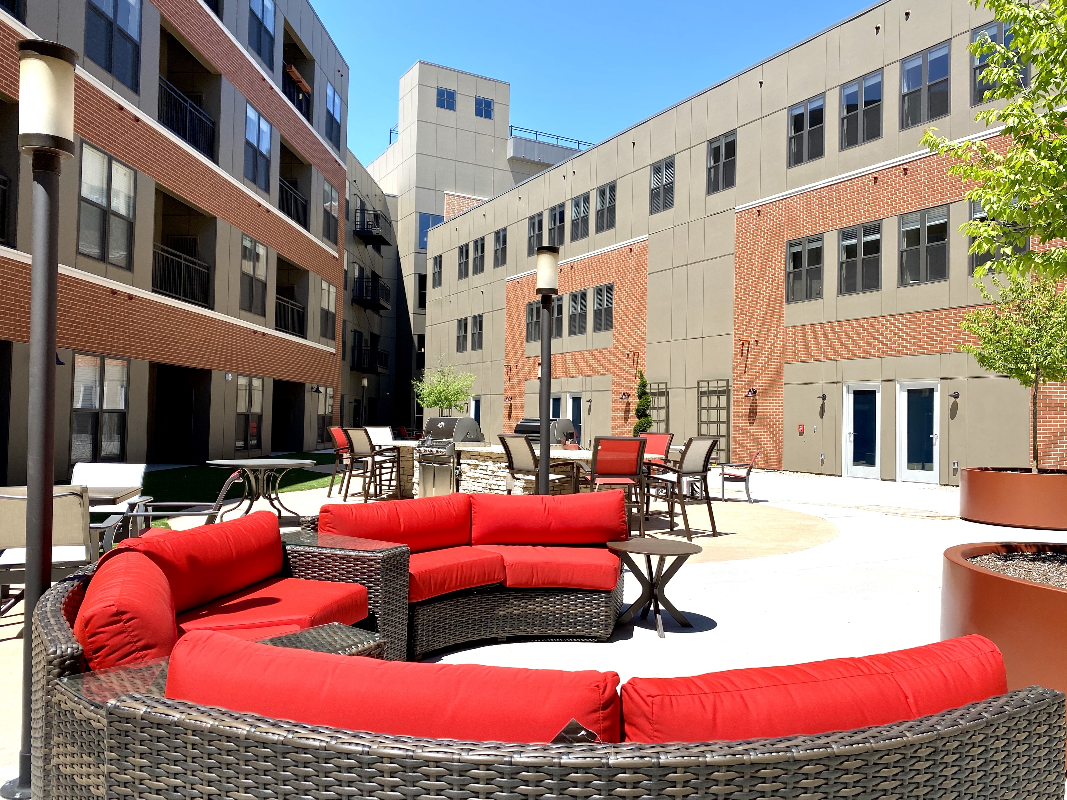 Modern apartment courtyard with stylish red wicker seating and a spacious gathering area, set against sleek building architecture.
