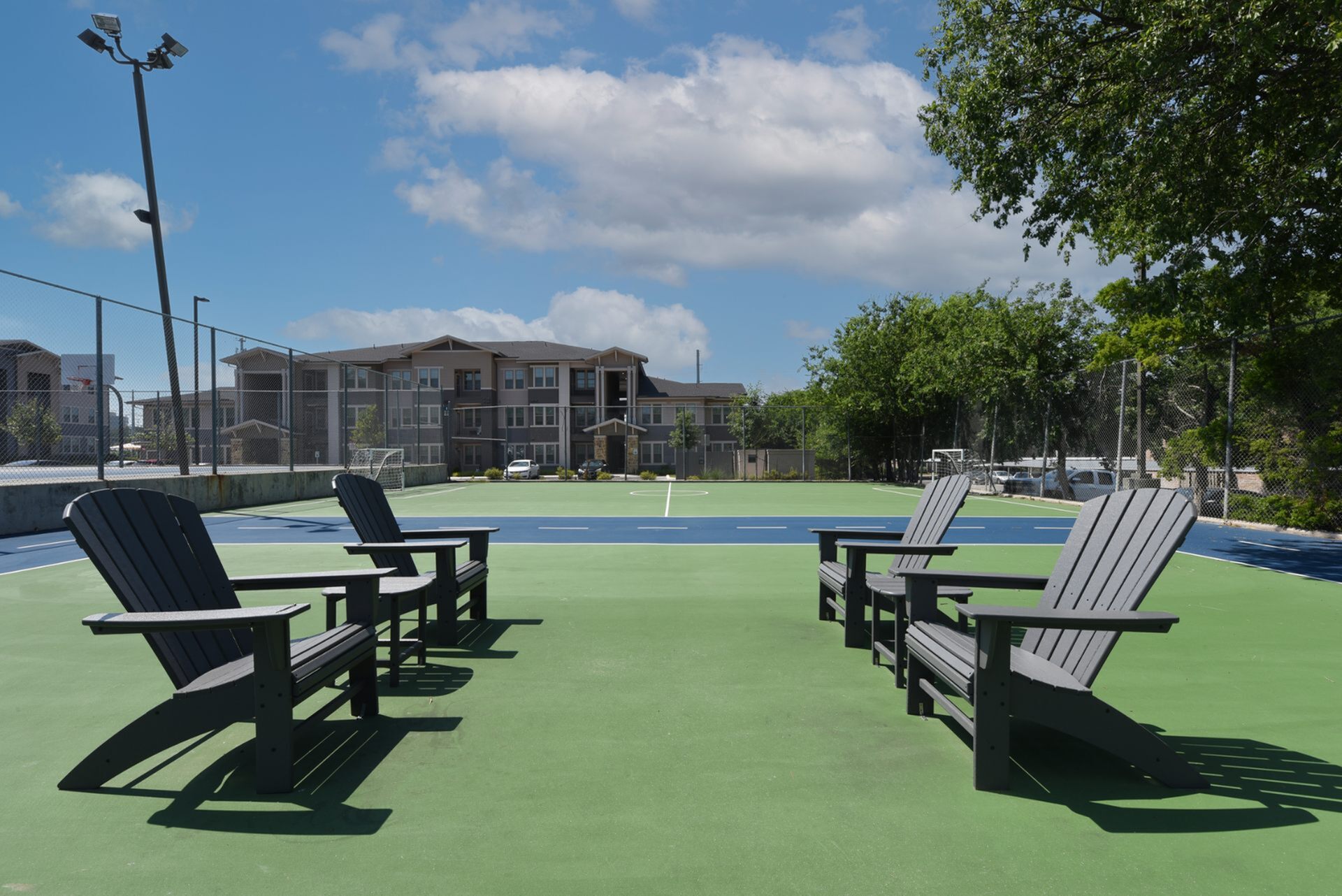 Vibrant recreational area featuring a modern sports court with seating, set against a backdrop of alluring apartment buildings and lush greenery.