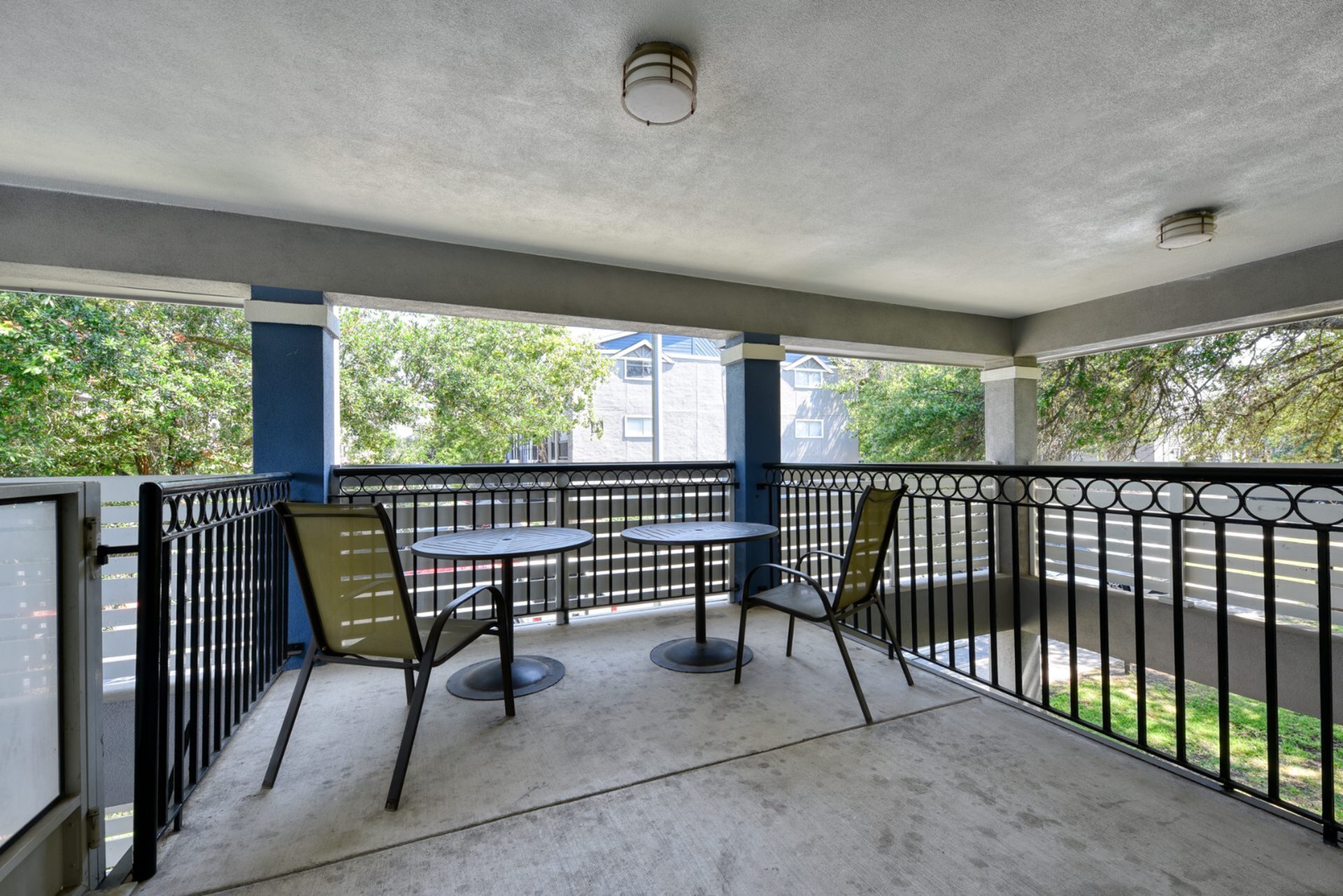 Charming covered balcony featuring two circular tables and chairs, perfect for relaxing with a scenic view of lush greenery.