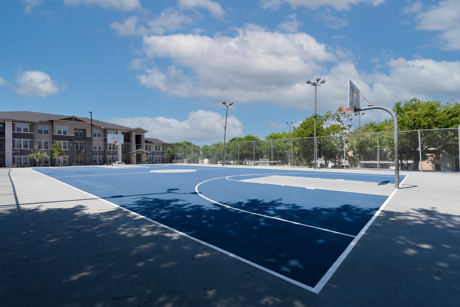 Spacious outdoor basketball court next to modern apartments under a bright blue sky.
