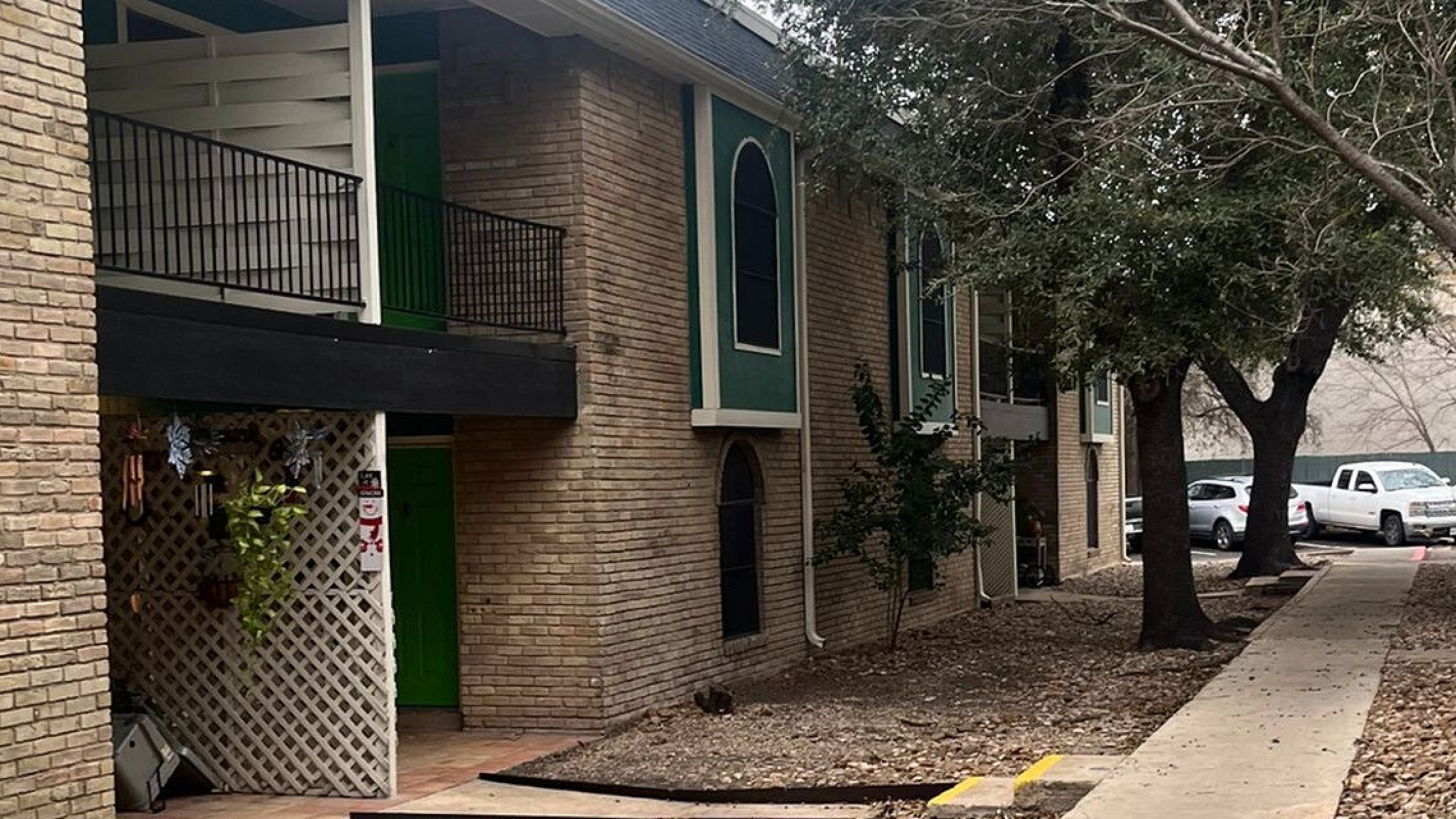 Charming apartment exterior with brick facade, lush trees, and a well-maintained walkway.