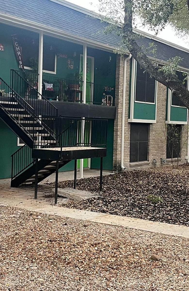 Charming apartment complex with vibrant green facade, set amidst mature trees and inviting outdoors.
