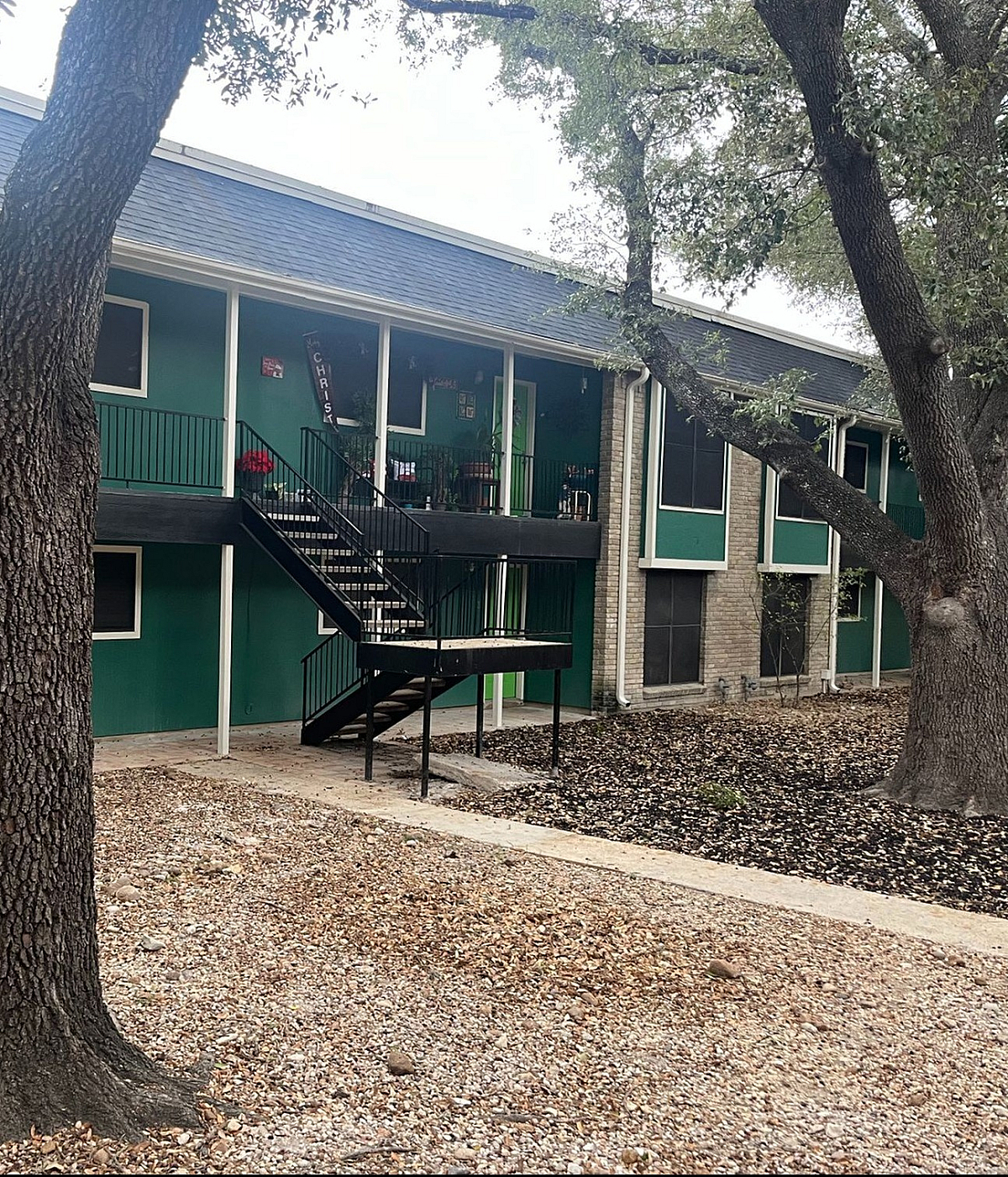 Charming apartment building with vibrant green accents and spacious balconies nestled among mature trees, offering a serene living environment.