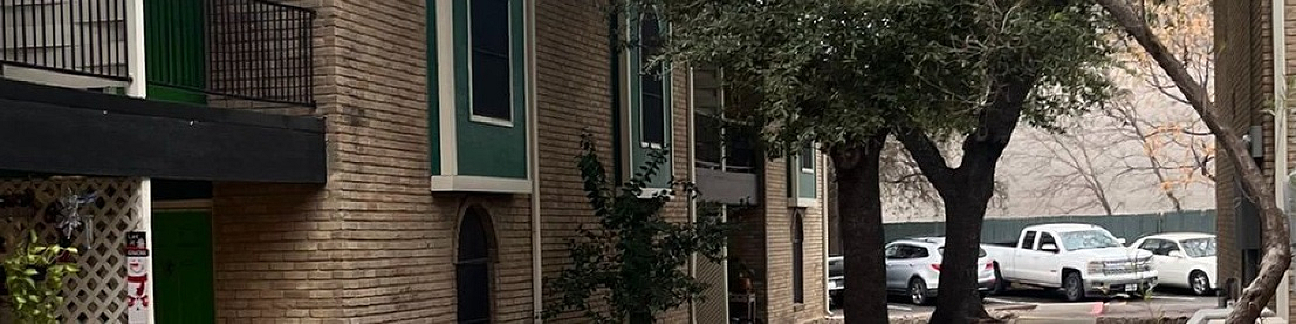 Charming apartment complex with beautiful green facade and welcoming pathway, surrounded by natural landscaping and mature trees.