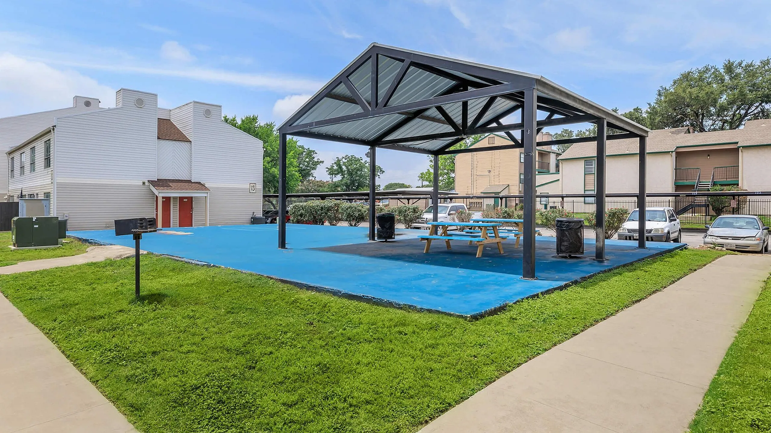 Inviting outdoor area with a modern gazebo, picnic tables, and vibrant blue flooring, perfect for gatherings in a charming residential community.