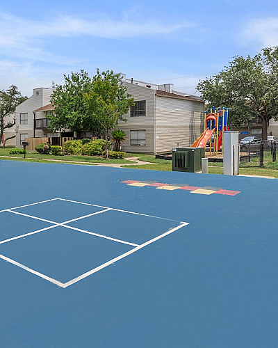 Inviting communal space featuring a spacious blue court, covered seating area, and vibrant children's playground, ideal for family gatherings and outdoor fun.
