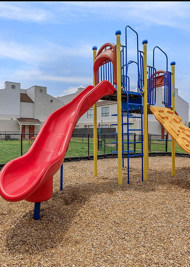 Vibrant playground with a bright red slide and climbing structure, set against modern residential apartments.
