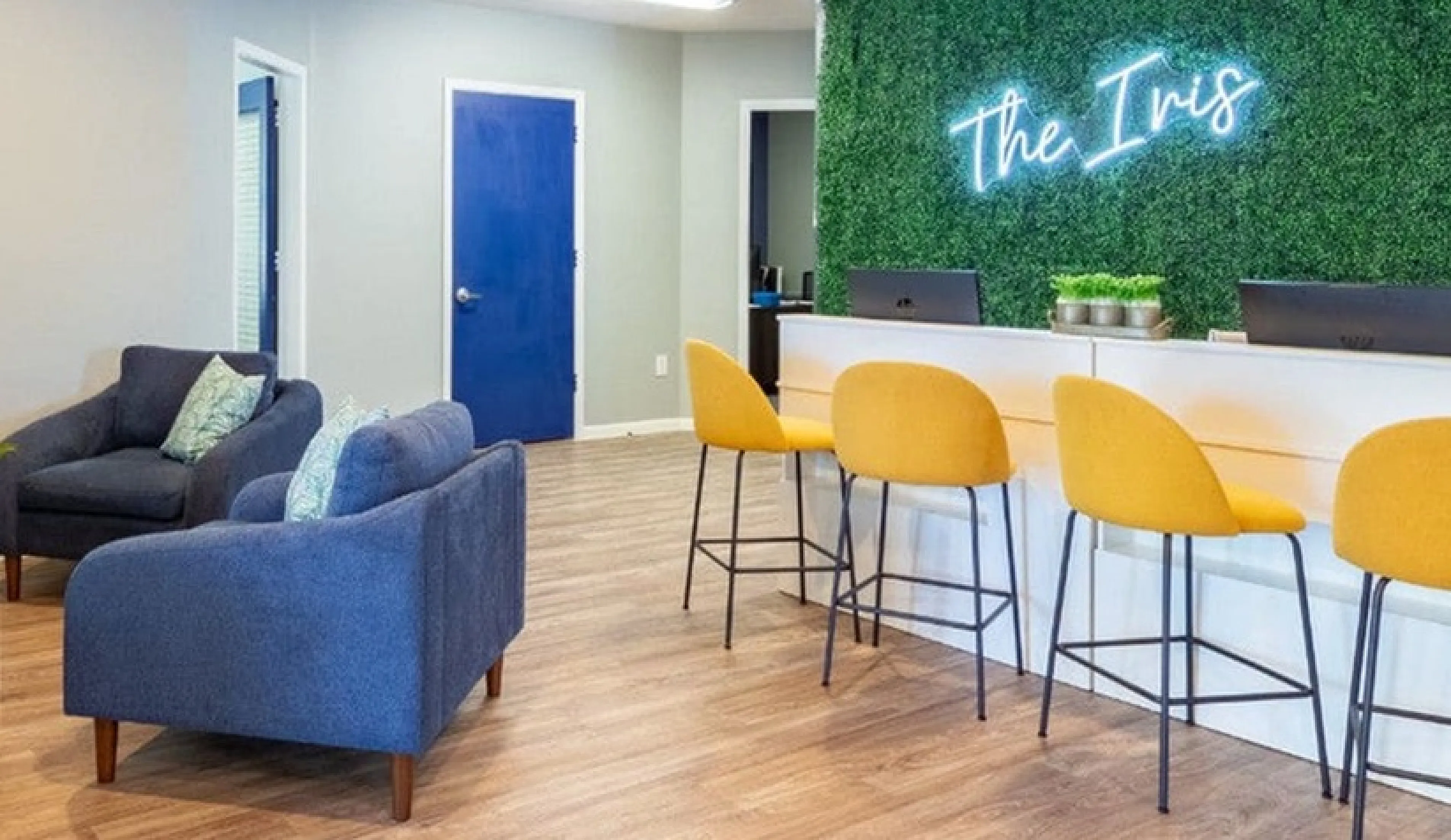 Chic and modern lobby featuring plush blue seating, a stylish reception counter with vibrant yellow chairs, vibrant artwork, and a lush green wall under soft lighting.