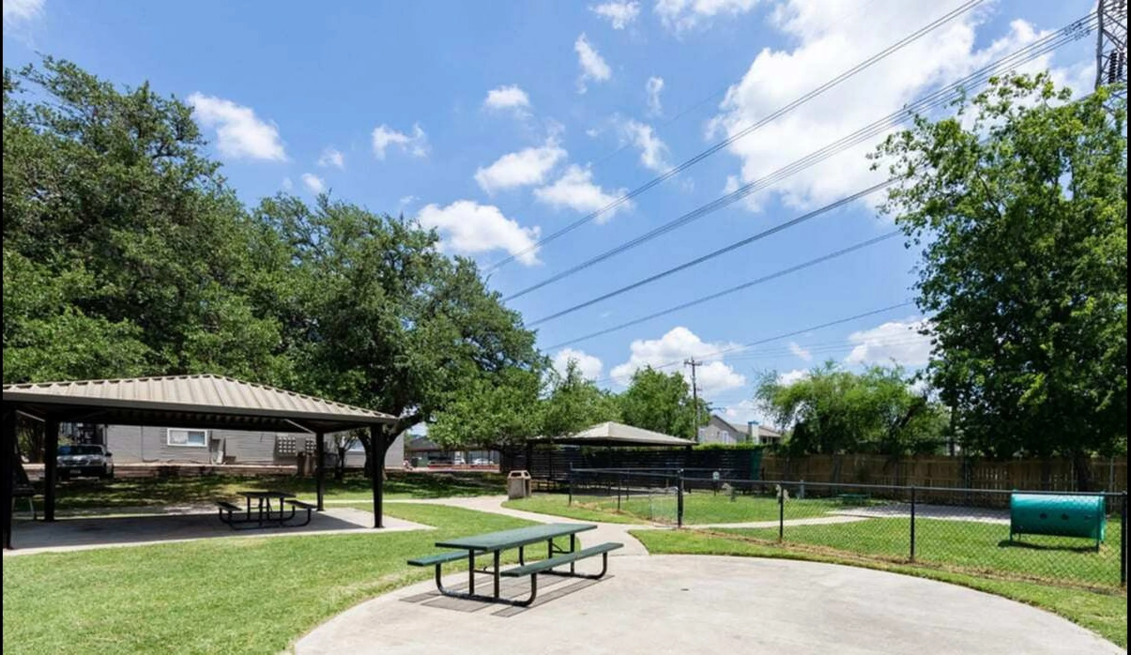 Inviting outdoor community area with picnic tables under shaded gazebos, surrounded by lush greenery and clear blue skies.
