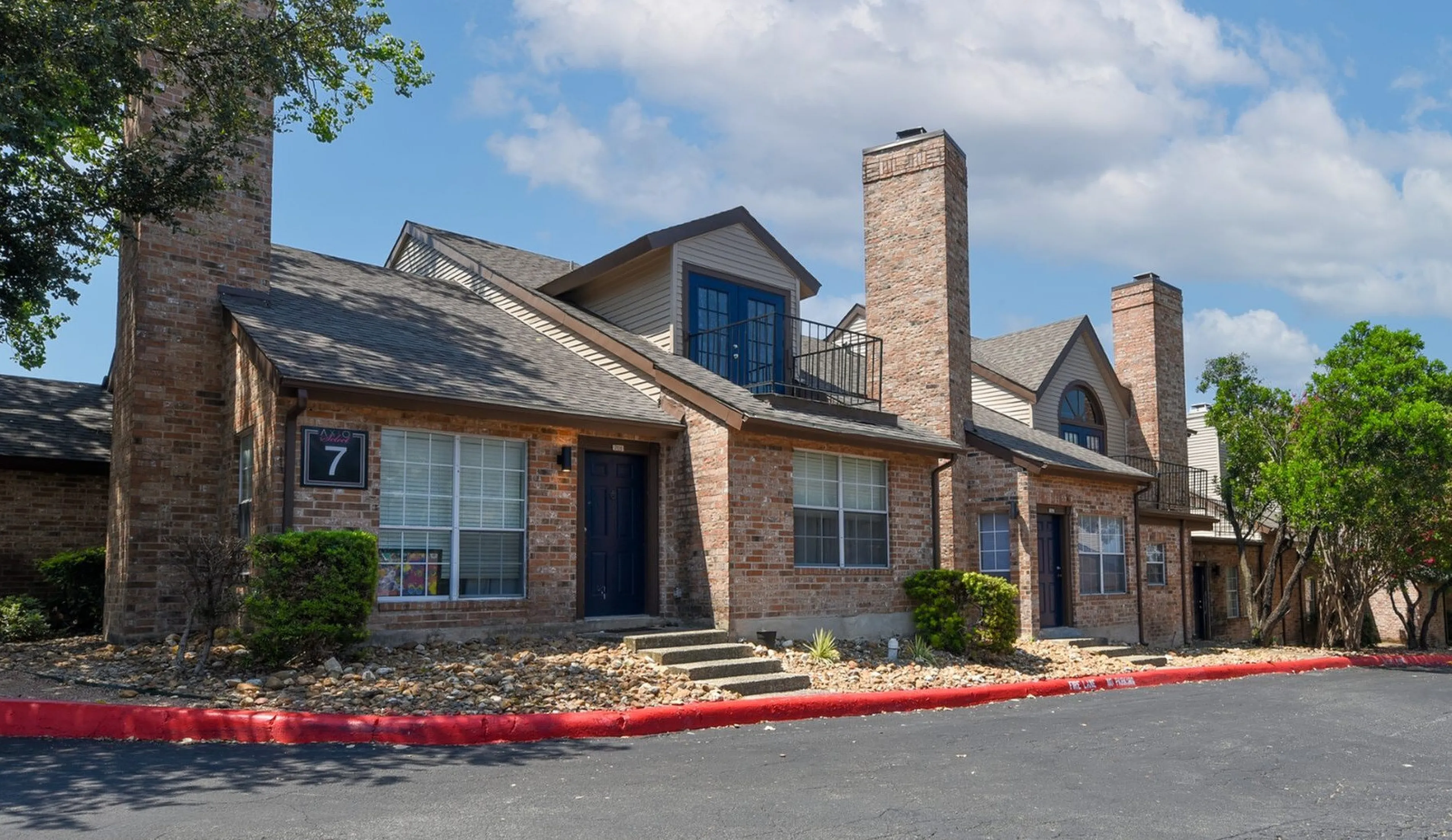 Charming brick apartment complex with tall chimneys, nestled in a serene neighborhood under a clear blue sky.