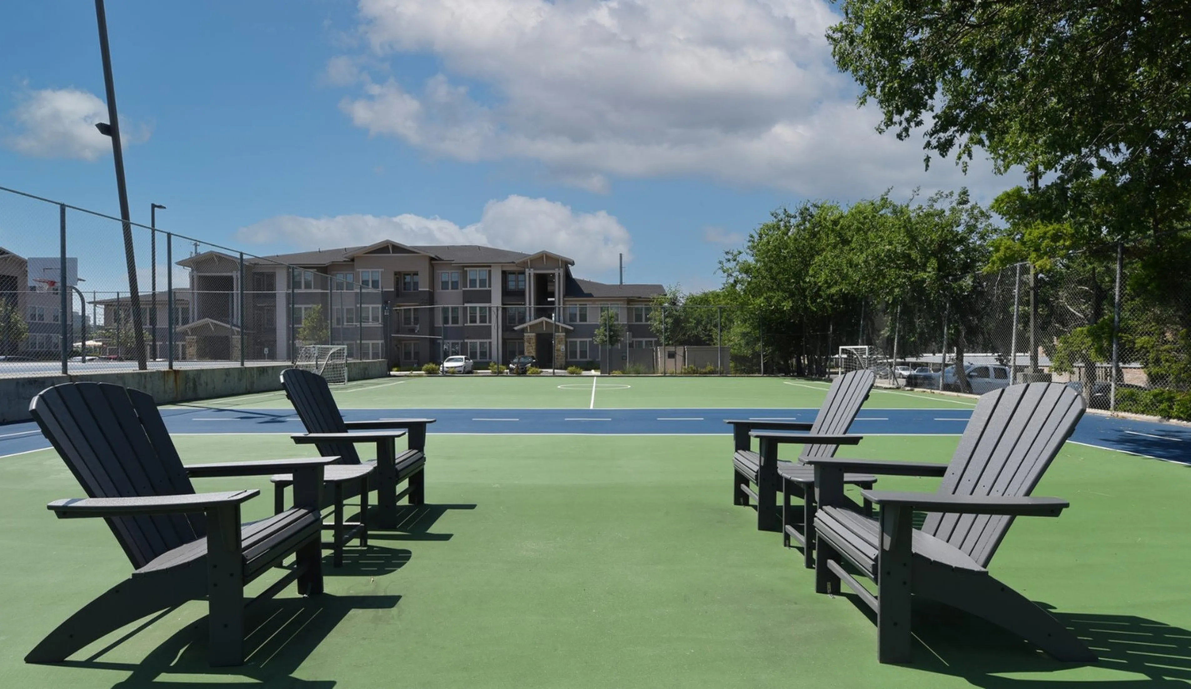 Inviting outdoor sports court with cozy Adirondack chairs, perfect for relaxation and leisure in a modern apartment community.
