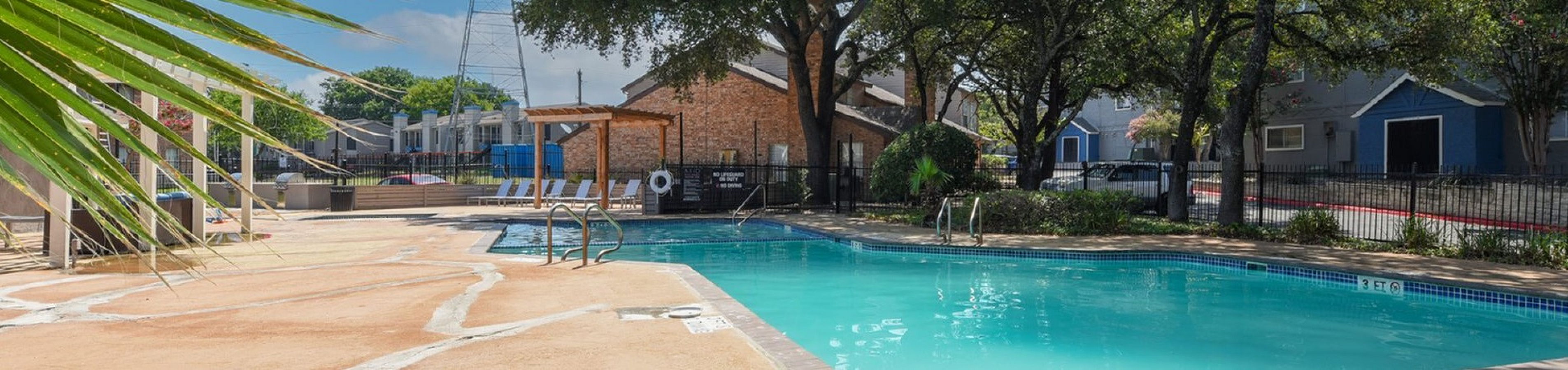 Inviting outdoor pool area with sun loungers and greenery, perfect for relaxation under the blue sky.