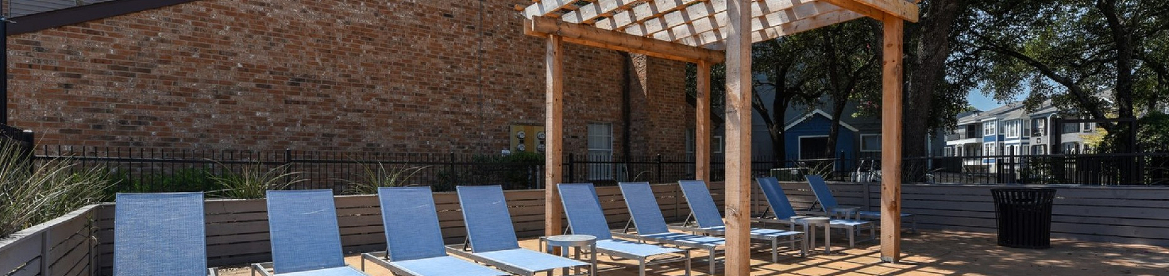 Inviting outdoor lounging area with stylish blue sun chairs under a wooden pergola, perfect for relaxation.