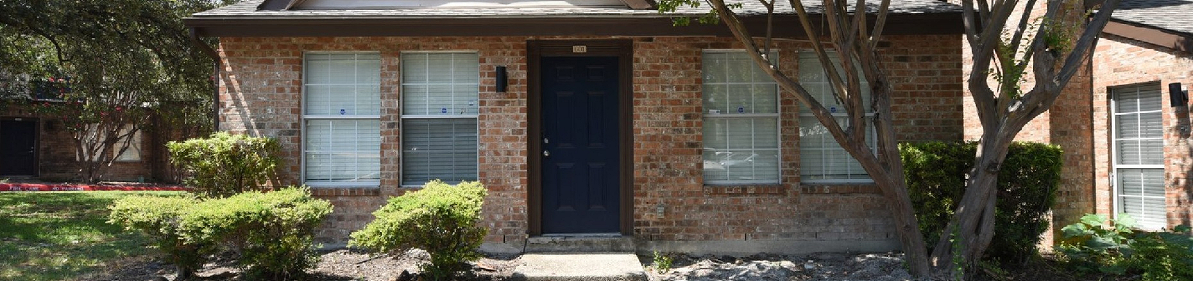 Charming brick townhouse with natural landscaping and a welcoming entryway, nestled in a serene neighborhood setting.