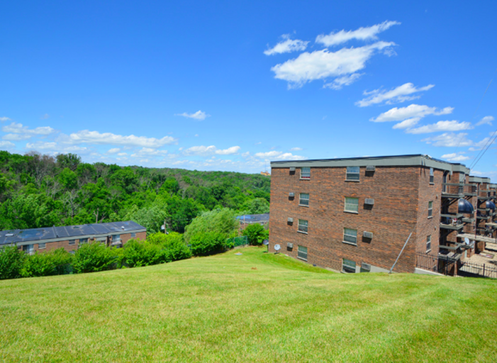 Inviting apartment complex with stunning views of lush greenery and clear blue skies, offering tranquility and modern living.