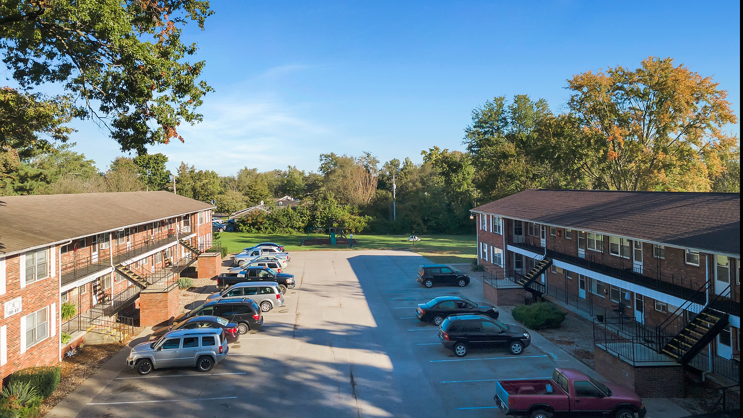 Inviting apartment complex with ample parking, lush landscaping, and vibrant blue skies, offering a serene and welcoming environment.