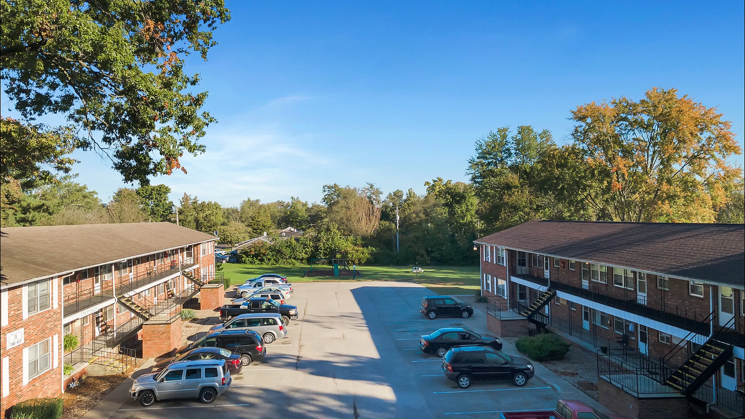 Sunlit apartment complex with welcoming greenery and ample parking spaces.